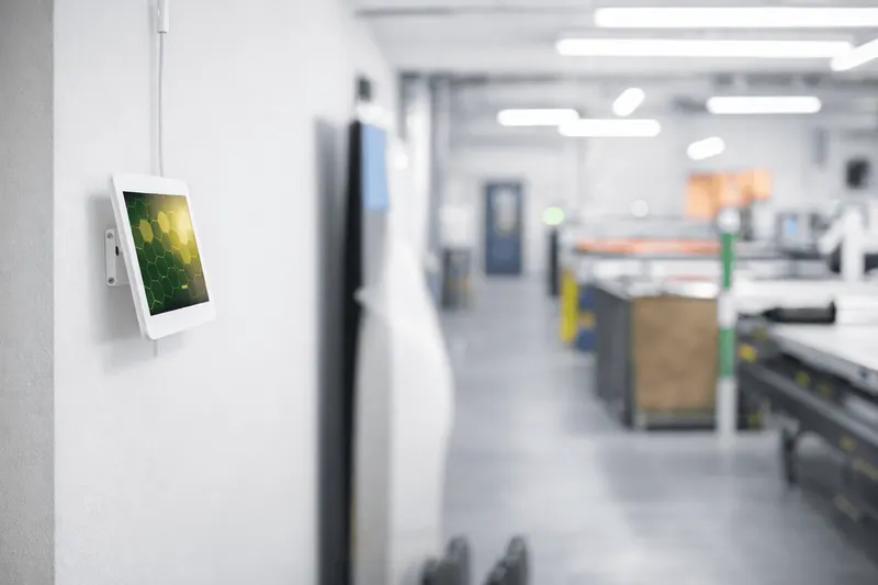 ChimeHive clock-in kiosk on a wall-mounted tablet beside the production floor of a manufacturing workshop